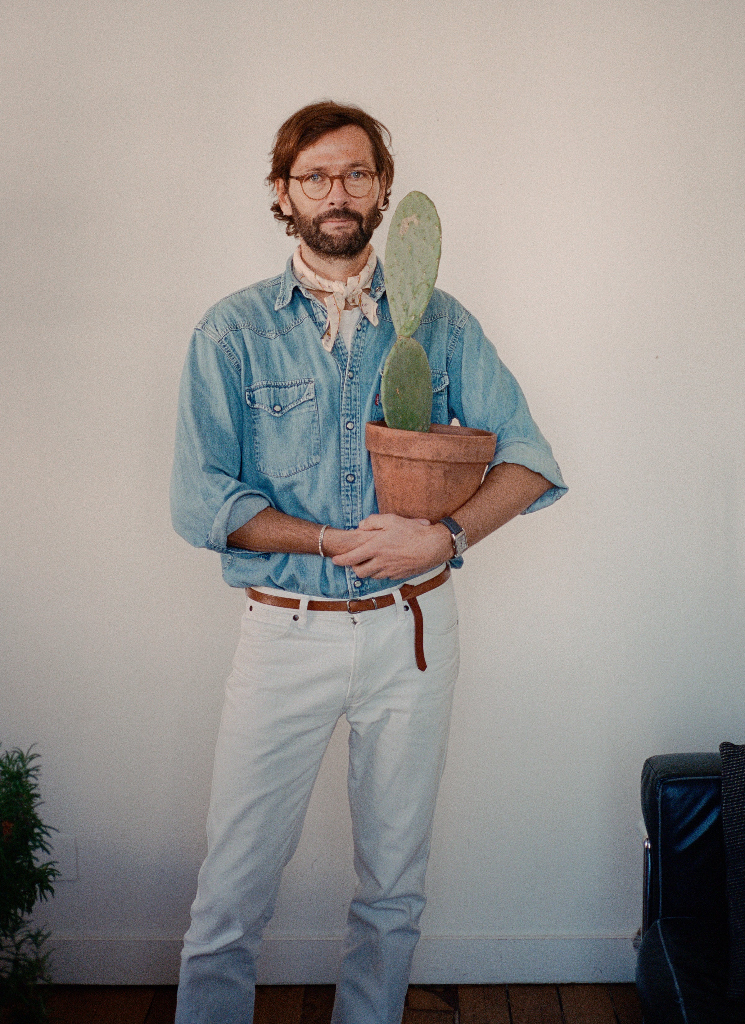 Mathias standing in front of the white wall holding a pot of cactus in a terracotta pot.