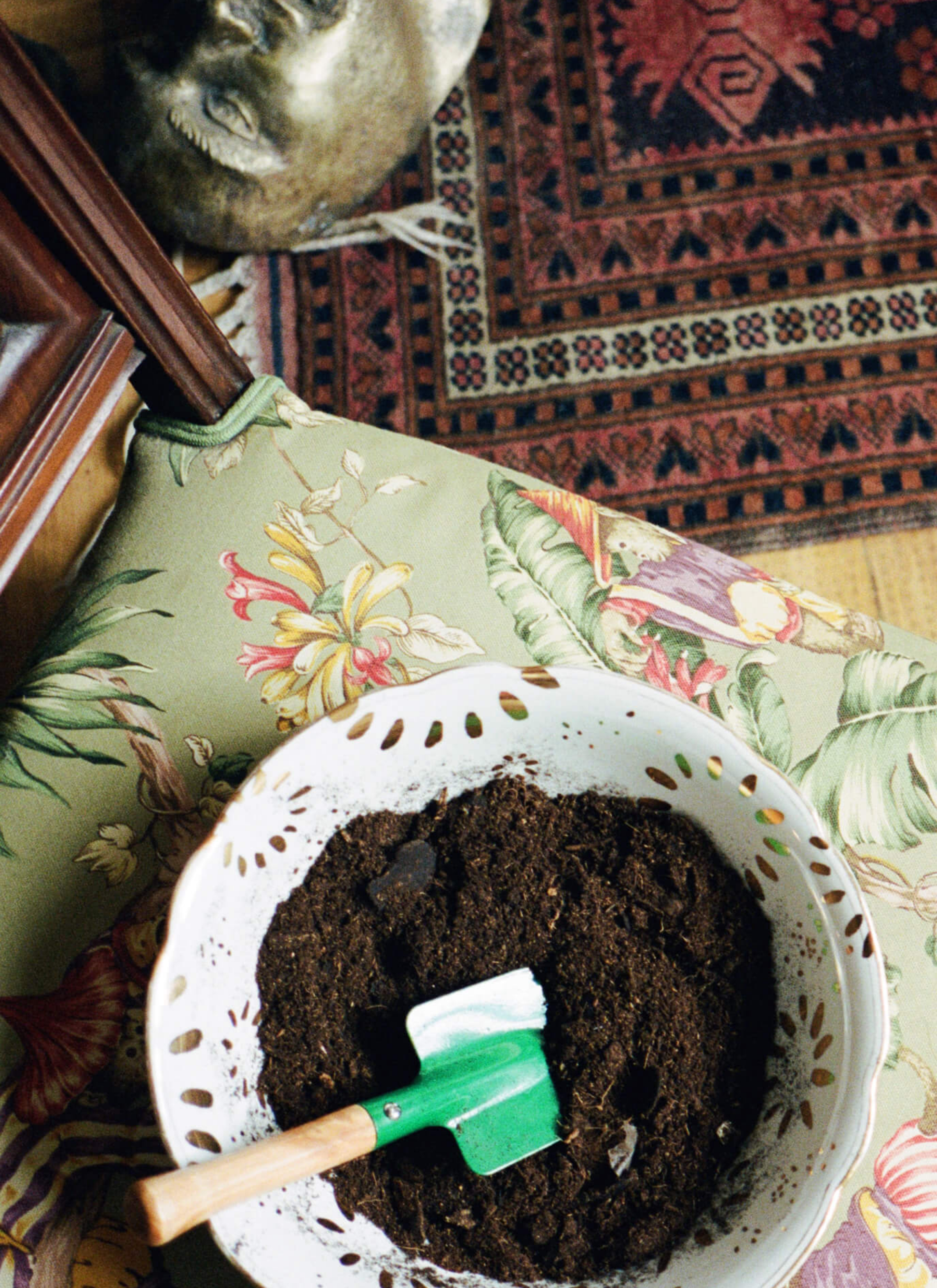 A bowl filled with soil and a trowel left on the chair that has a floral cover.