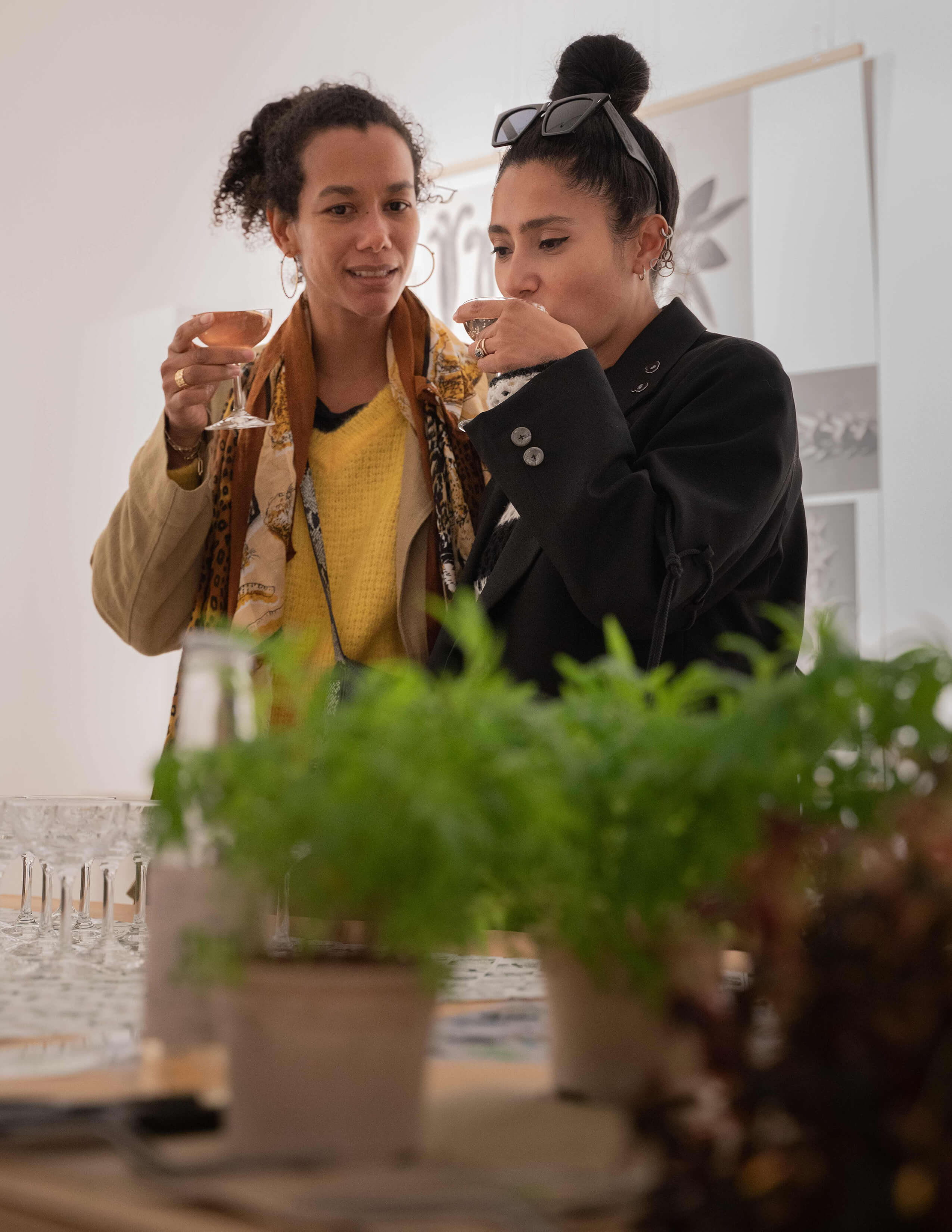 Two ladies are having their drinks while browsing plants and other stuff that was presented on the table.