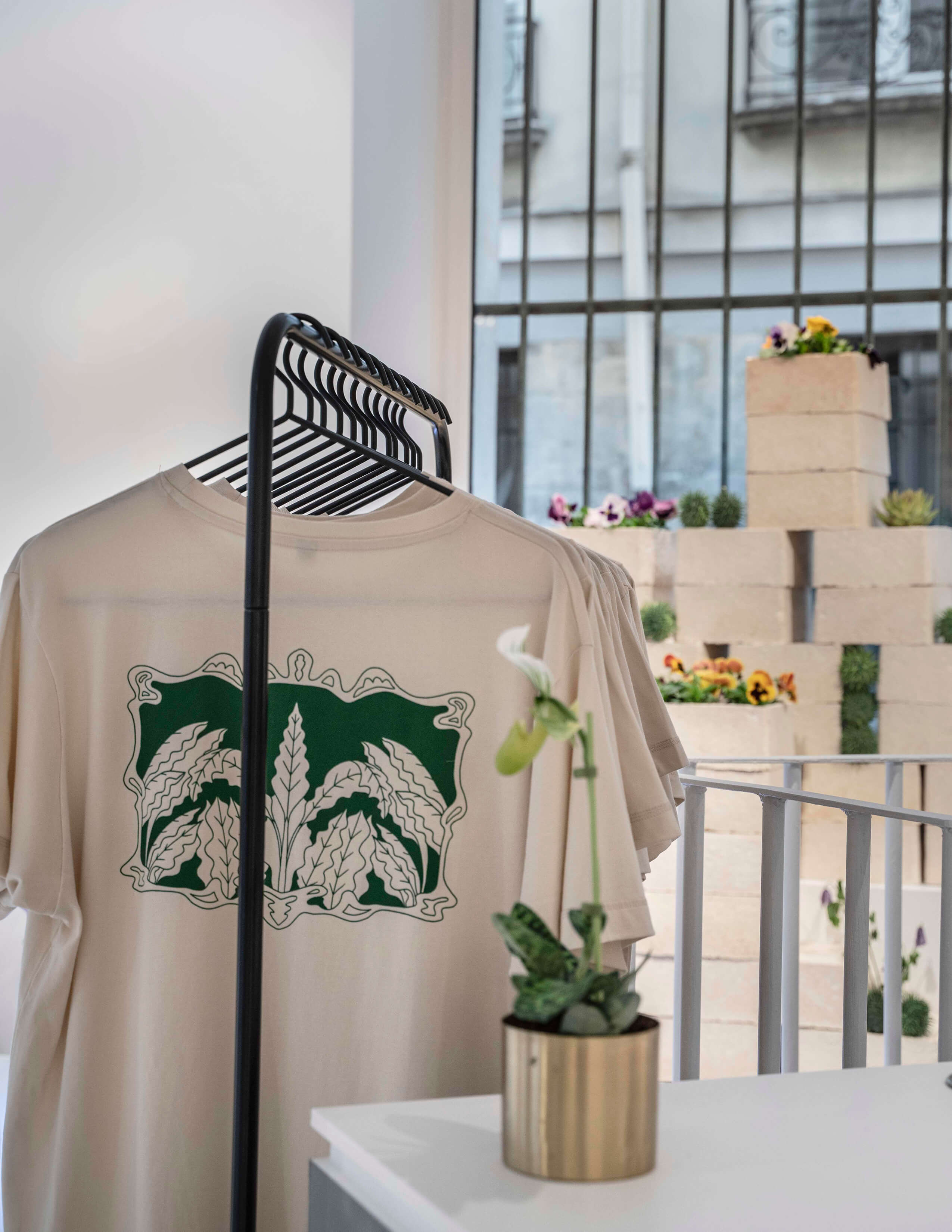 Sowvital merchandise - T-shirts are hung up on the clothing rack and there is a small pot of plant next to it.