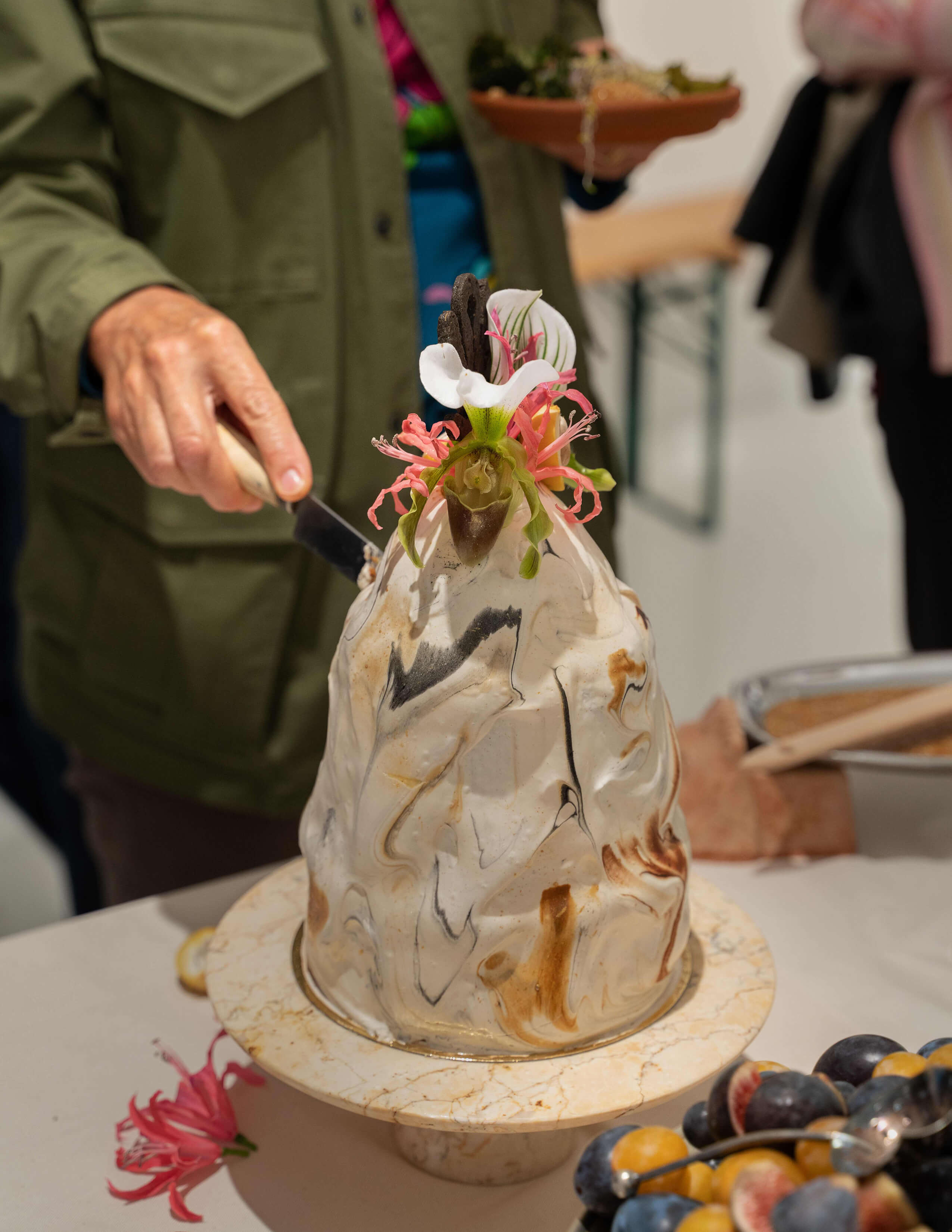A person held a knife to cut the artistic cake while holding a plate of food on the other hand.