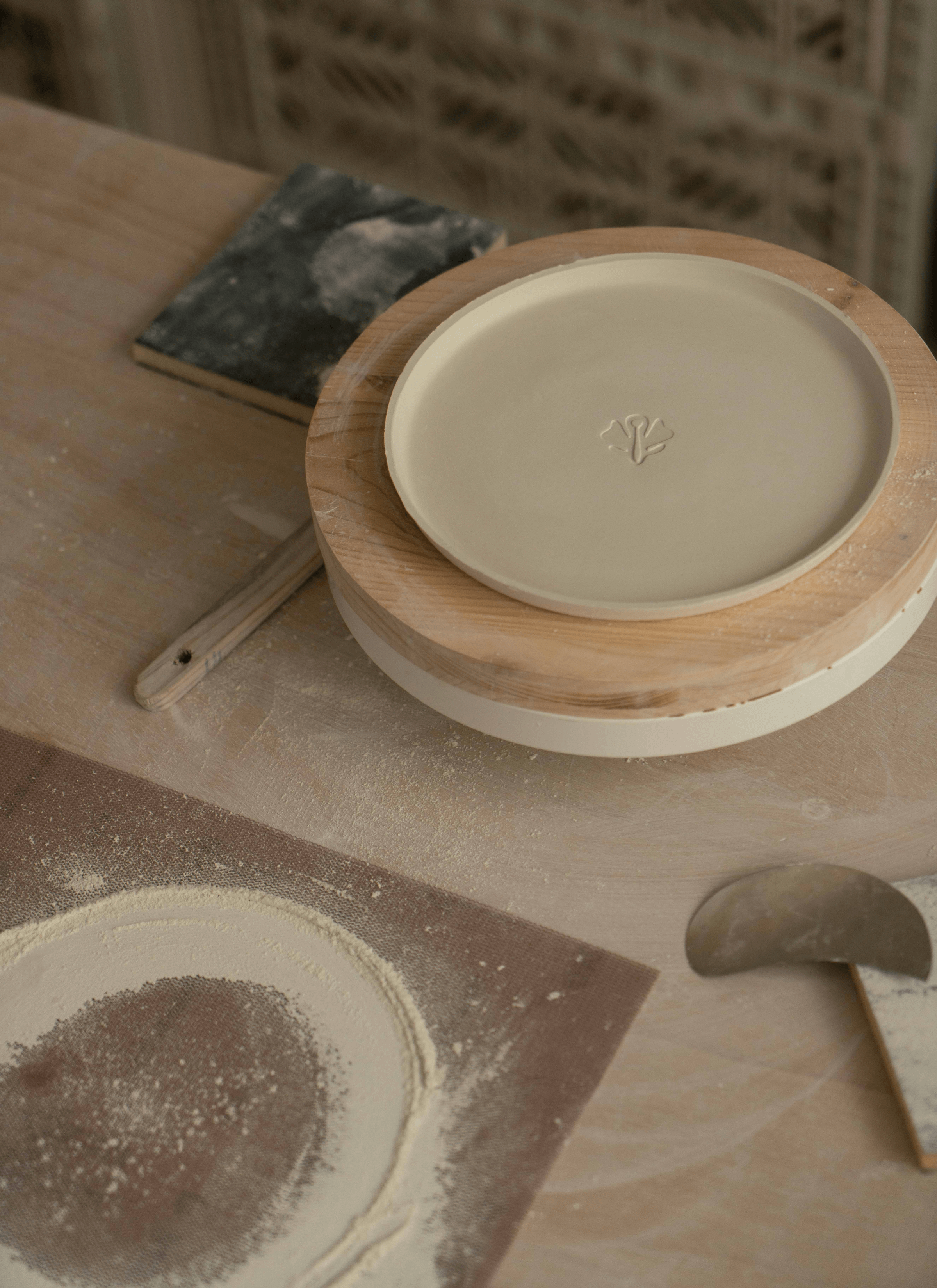 A table with a sand paper covered with the ceramic powder rubbed from ceramic projects, a saucer with Sowvital label on it and some other ceramic tools/gadgets spread out on the surface. 