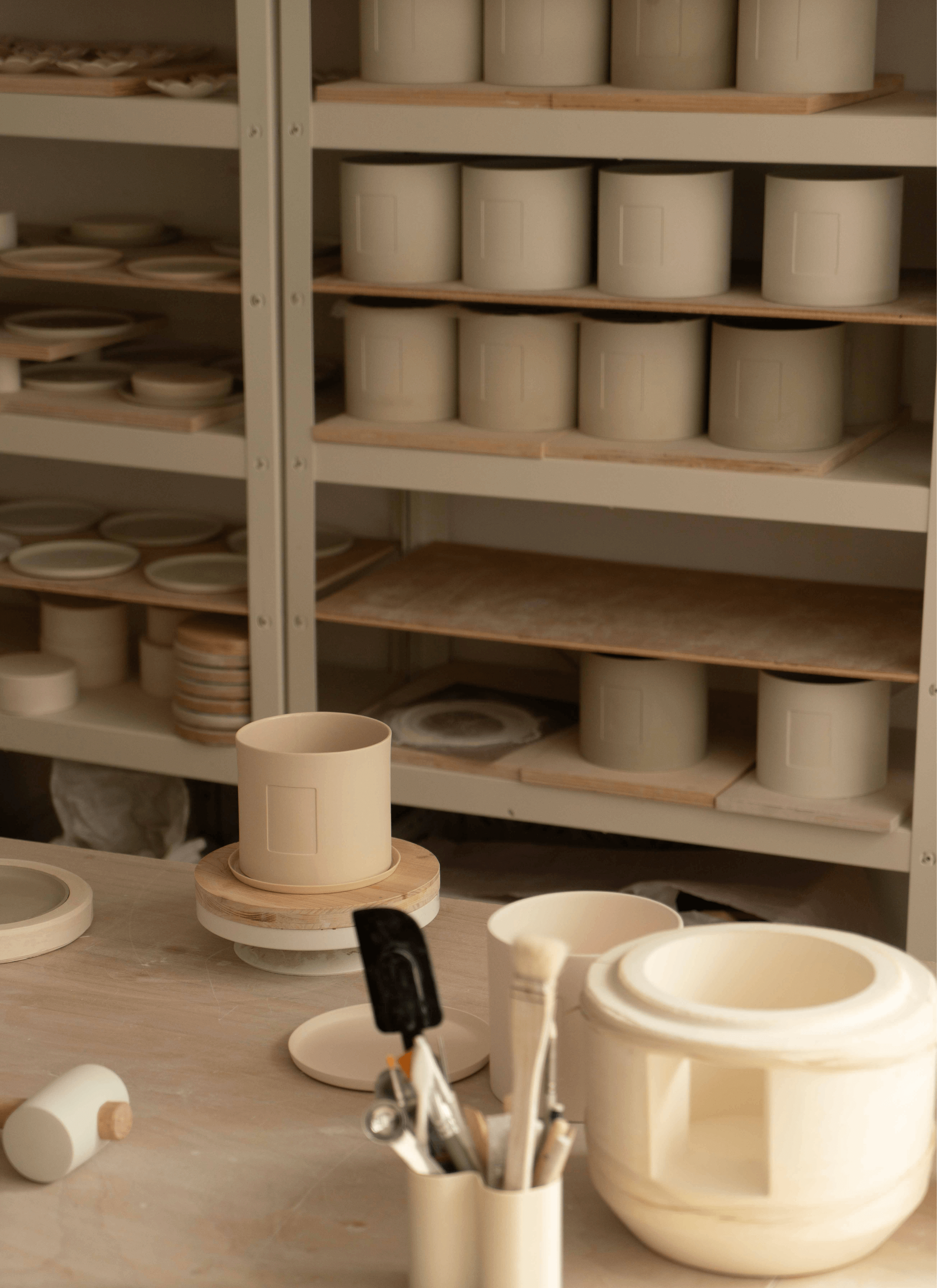 Tools and gadgets for ceramic laying out on the table with a shelf of ceramic pots, saucers and some flower shape germination disc on the shelf.