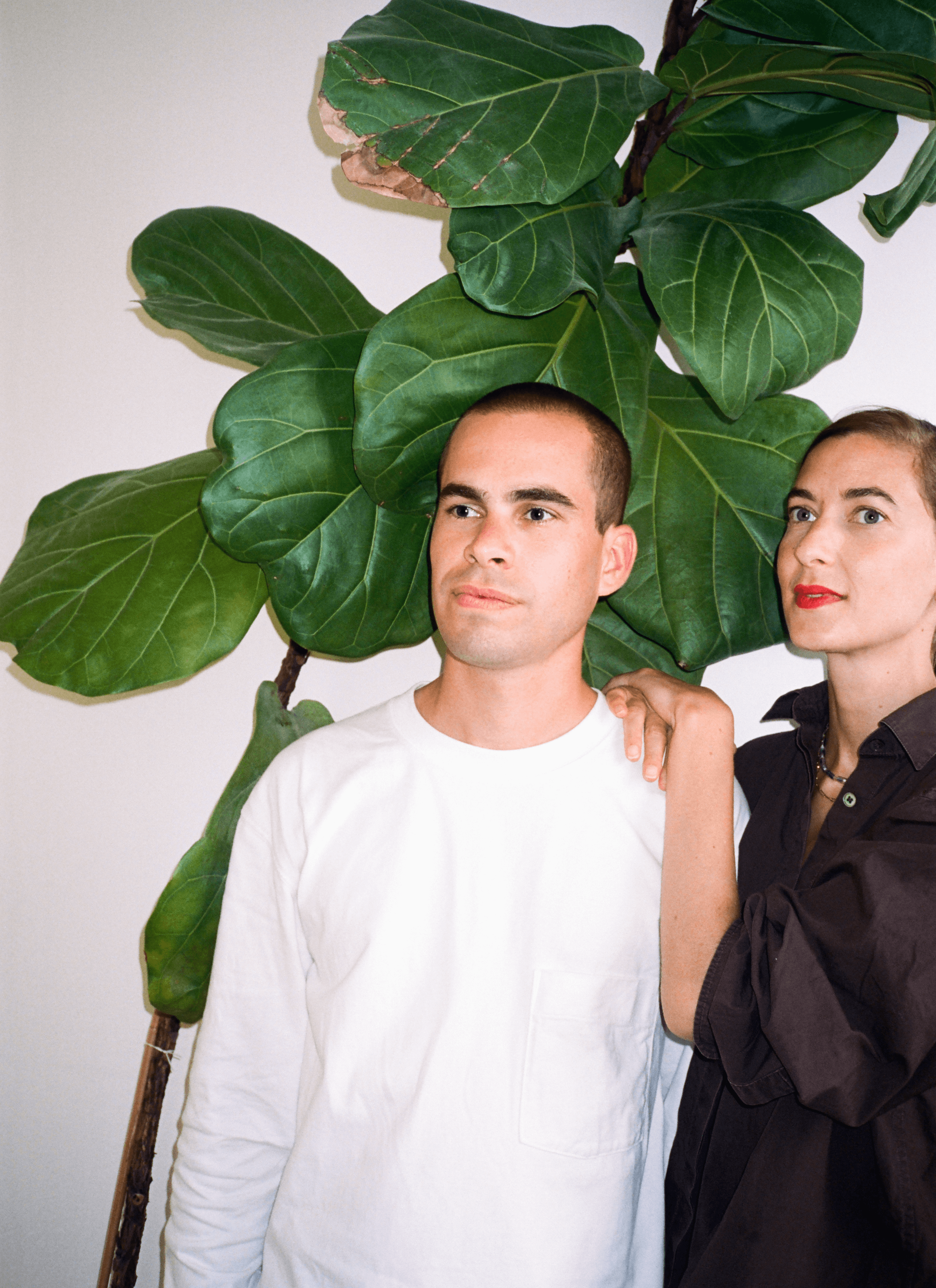 Margaux and Tristan standing in front of a significant fiddle-leaf fig in the background.