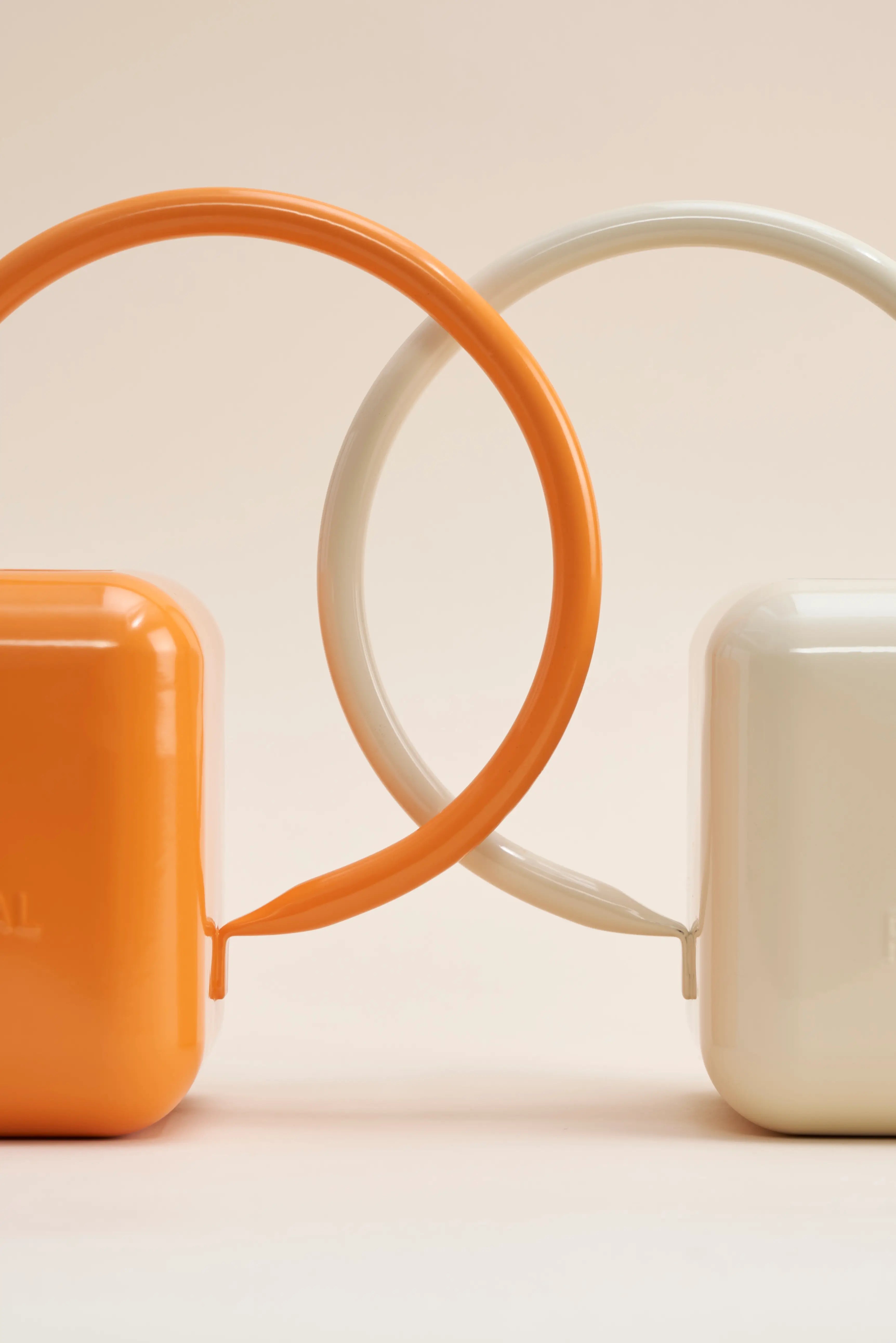 Two stainless steel watering cans sit back to back, one orange and one beige.