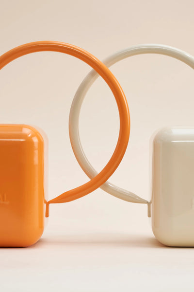 Two stainless steel watering cans sit back to back, one orange and one beige.