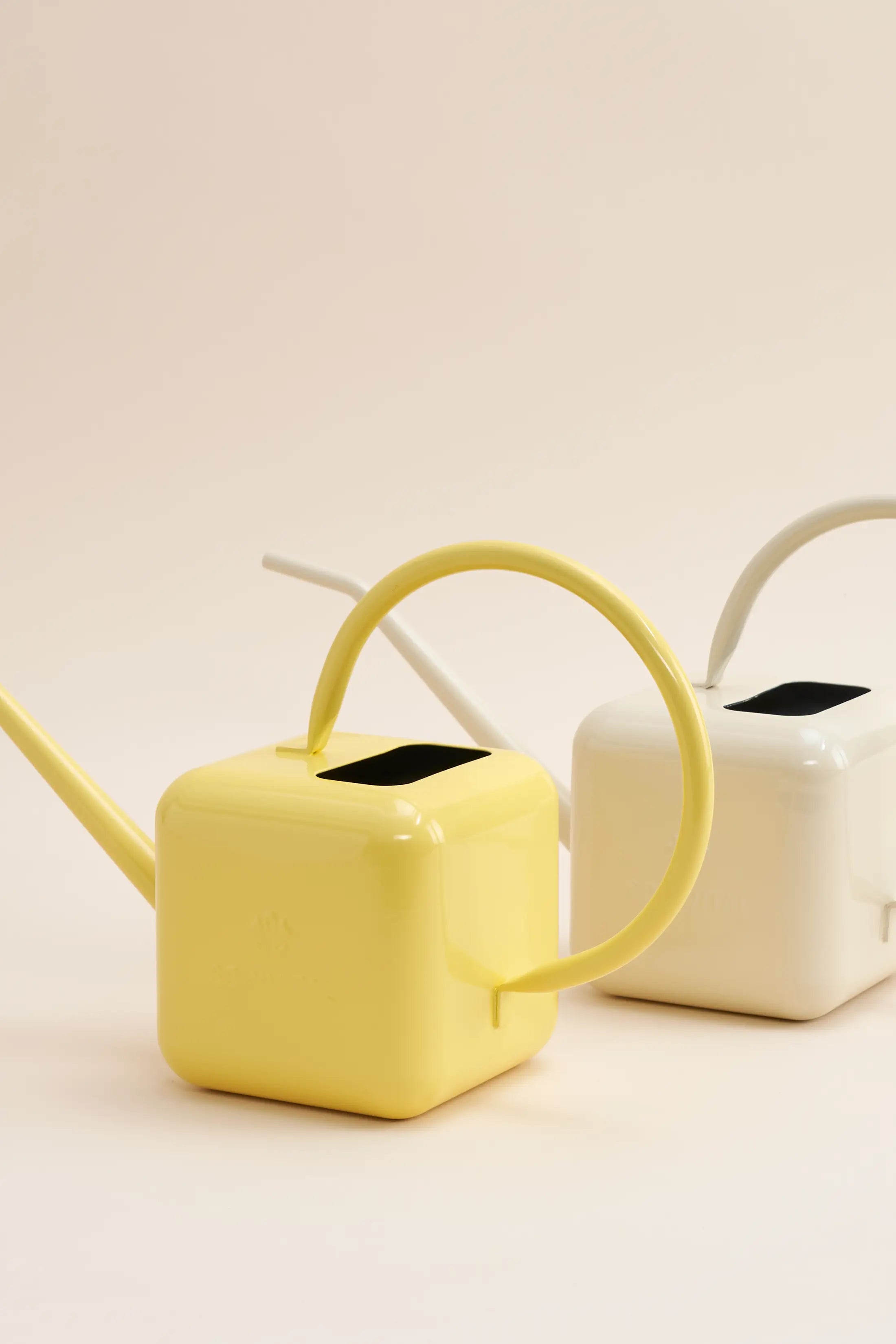 Two Sowvital watering cans. In the front there is a yellow watering can and behind is a beige watering can.