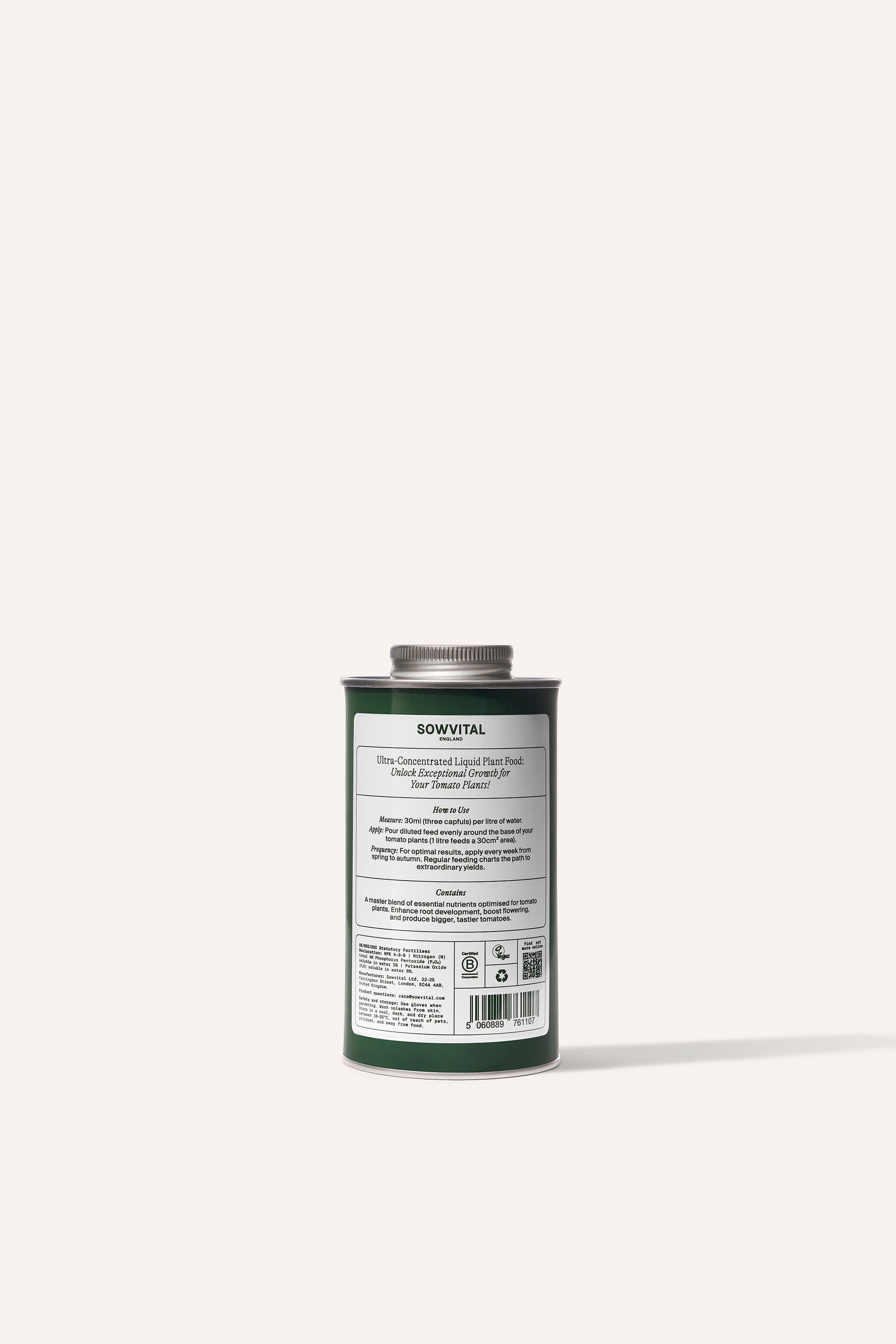 A tall round dark green metal tin of garden tomato plant fertiliser in front of a beige background.