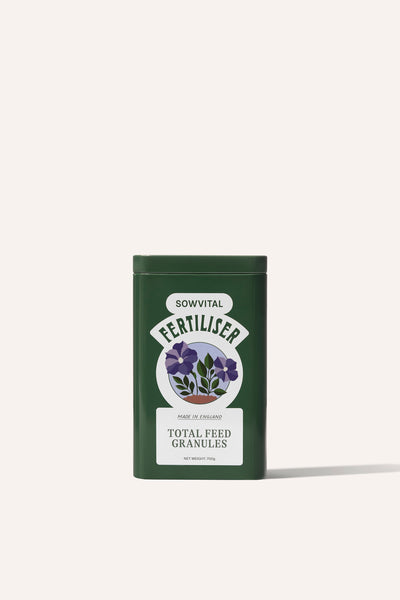 The front of a tall rectangular dark green metal tin of garden fertiliser granules on a beige background.