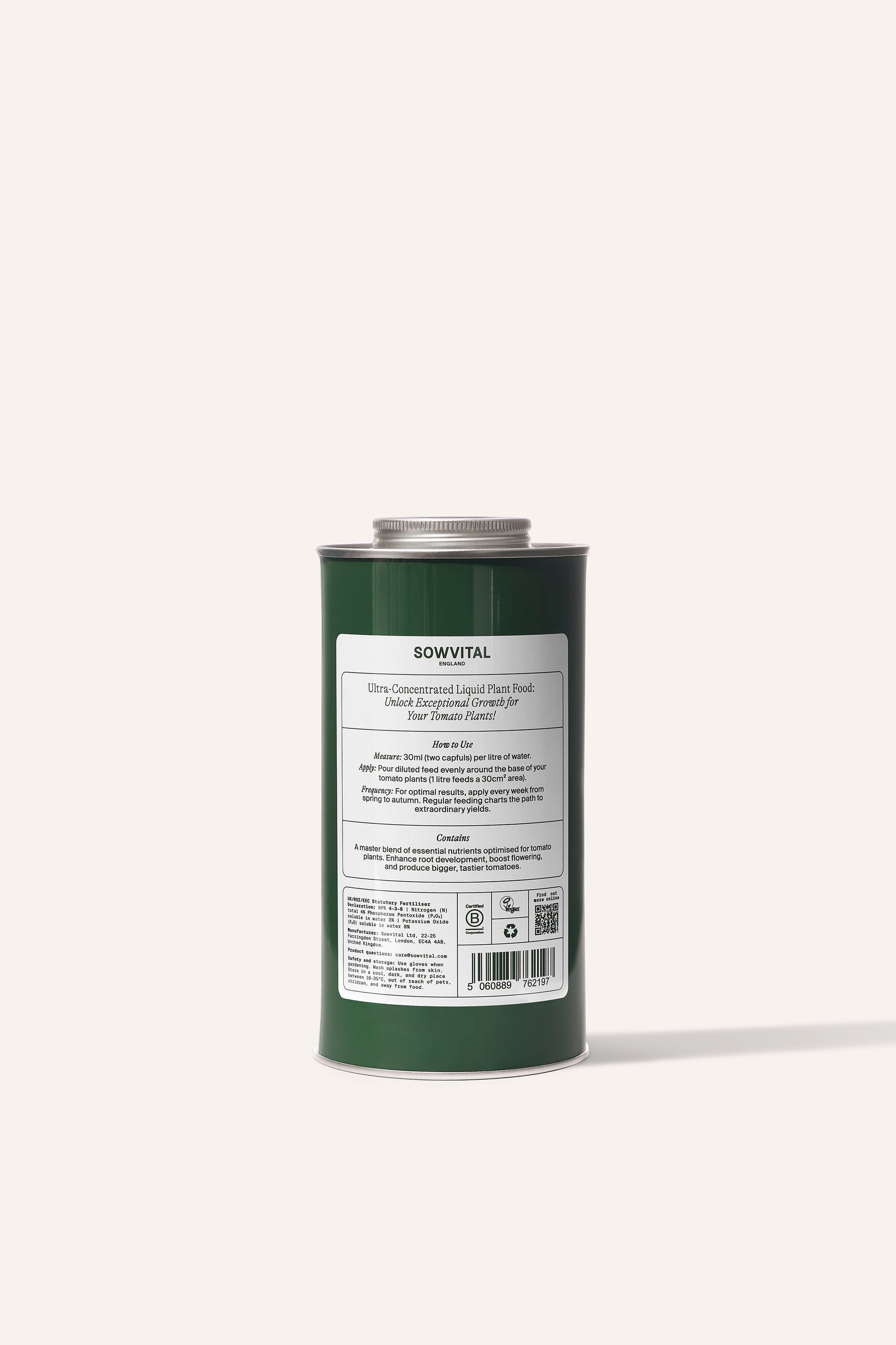 A tall round dark green metal tin of garden tomato plant fertiliser in front of a beige background.