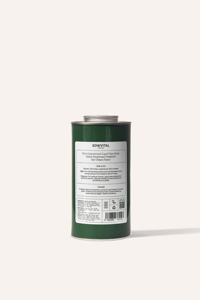 A tall round dark green metal tin of garden tomato plant fertiliser in front of a beige background.