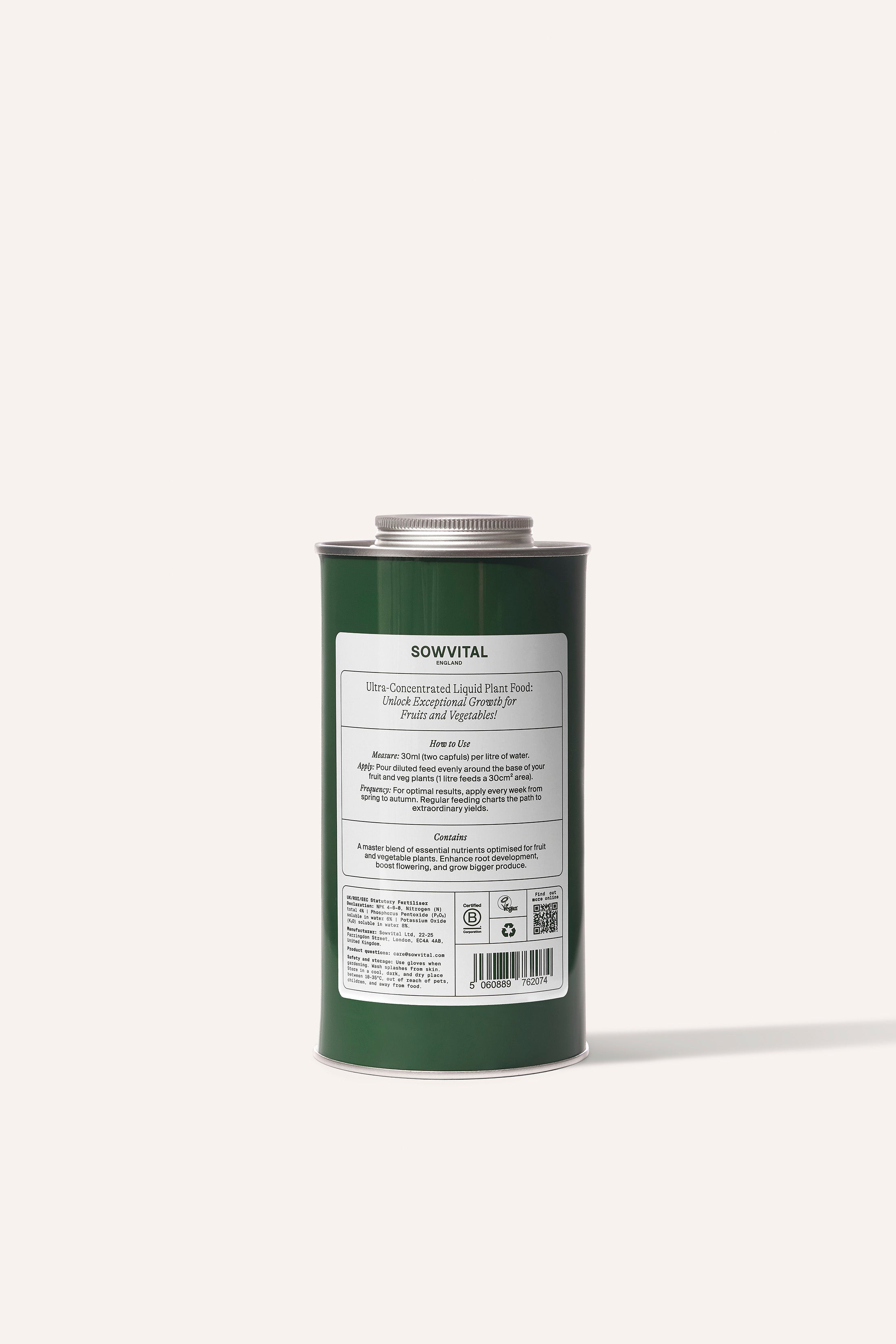 A tall round dark green metal tin of garden fruit & vegetable plant fertiliser in front of a beige background.