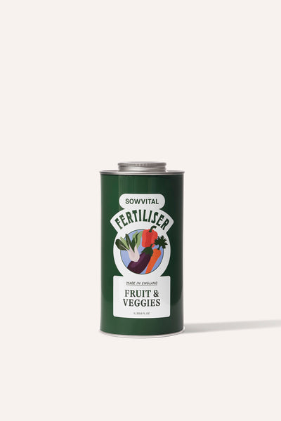 A tall round dark green metal tin of garden fruit & vegetable plant fertiliser in front of a beige background.