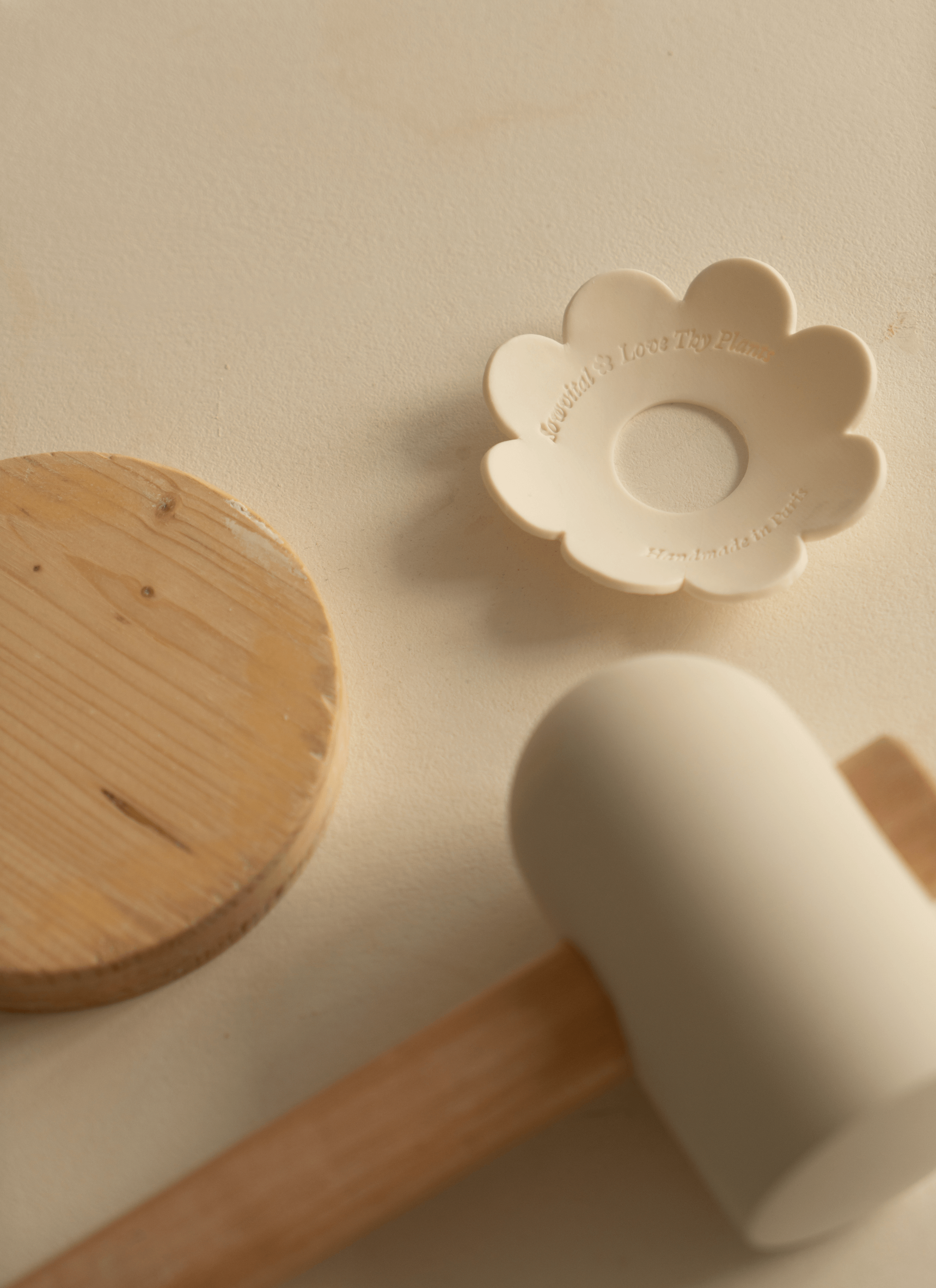 On the table, three distinct ceramic tools/gadgets are arranged: a hammer, a round wooden piece, and a germination disc adorned with Sowvital's label. Each tool serves a specific purpose in the ceramic-making process, from shaping to detailing.