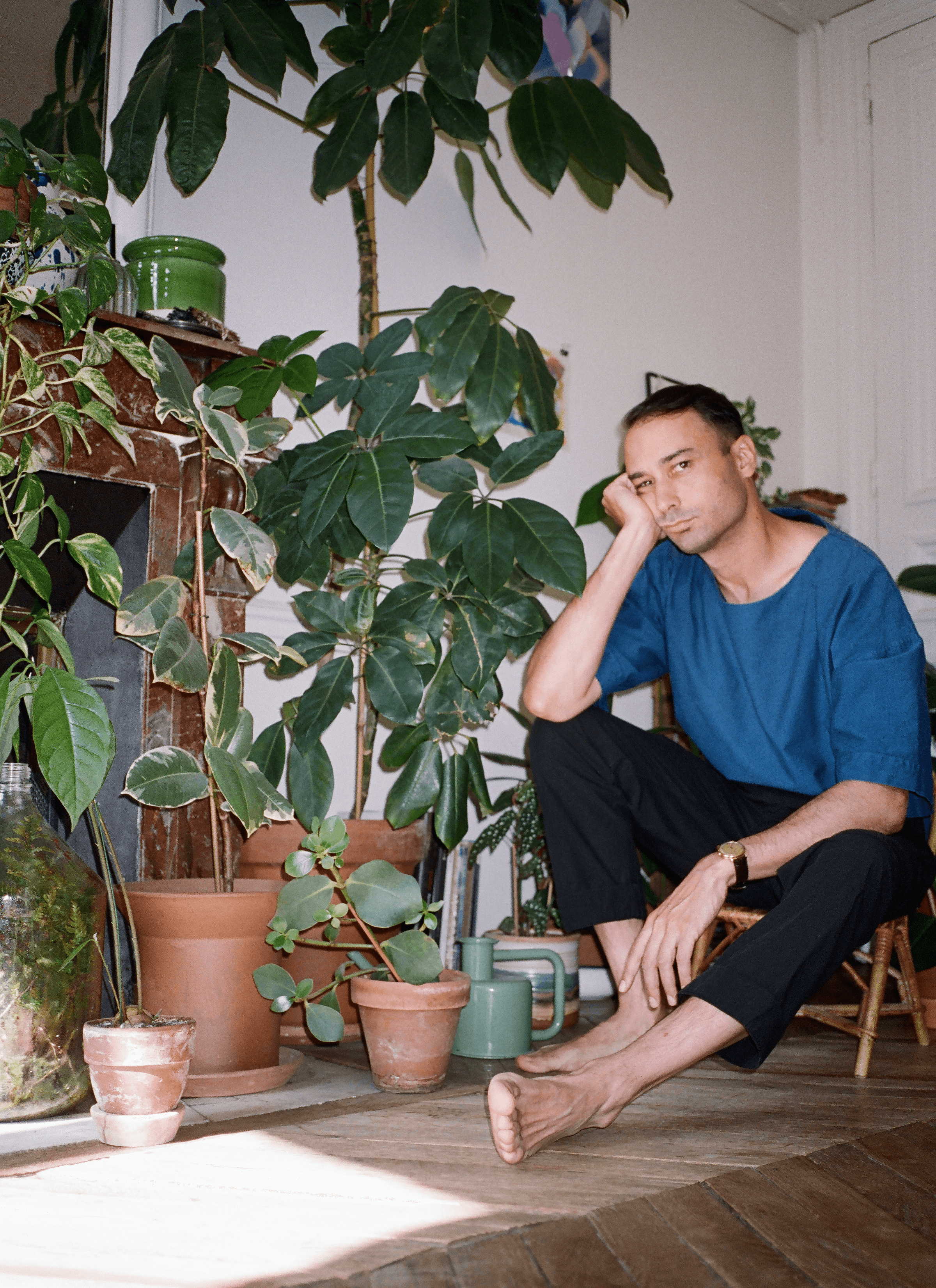 A photograph of Fred with his houseplant collections, a potted ficus elastica bineke, a potted Australian umbrella tree, Epipremnum marble queen, begonia maculata and a terrarium.