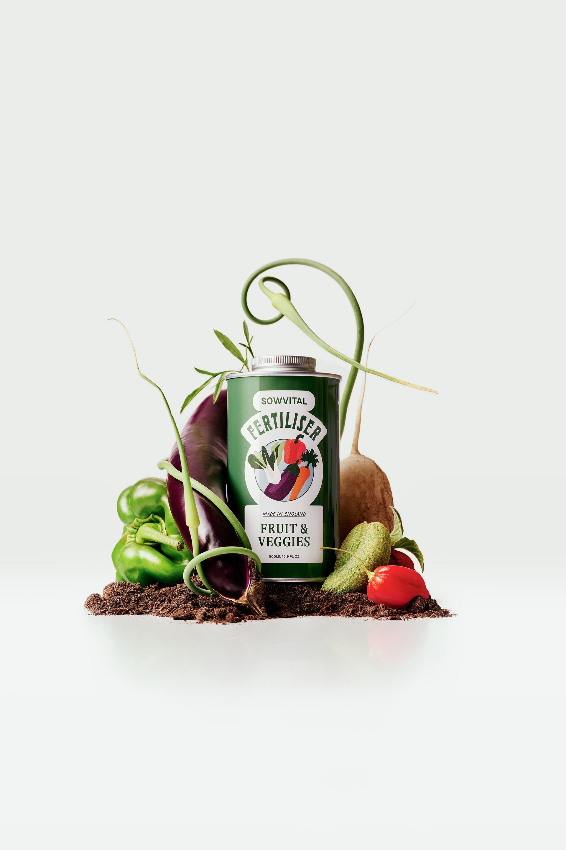 A dark green tin of Sowvital Fruit & Veggies fertiliser sits on a small mound of soil, surrounded by fruit and vegetables.