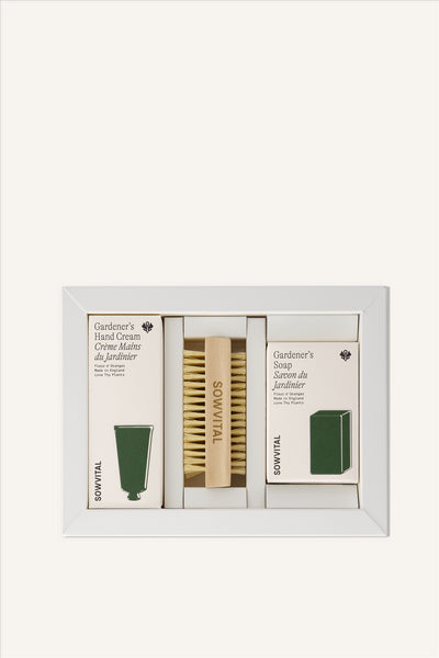 The contents of the Gardener's Hand Care Kit. 3 products sat in their boxes the internal box of the Hand Care Kit, The Gardener's Hand Cream, a wooden nail brush with "SOWVITAL" engraved into the side, and a bar of soap. The cream and soap are in beige fedrigoni boxes, with green illustrations of the shape of the product within. The background is beige.