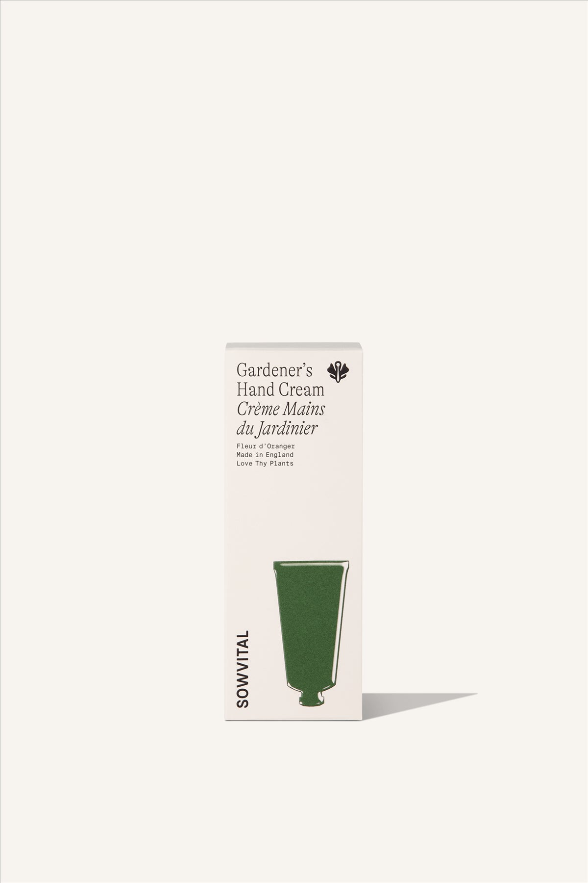 A tall rectangular fedrigoni paper beige box, with a green illustration of the shape of the hand cream tube within. The background is beige.