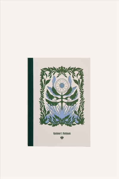 An A5 notebook with a beige cover and green cloth spine. The cover shows a green and blue illustration of a large, blooming flower, with a delicate botanical border. The background of the image is beige.