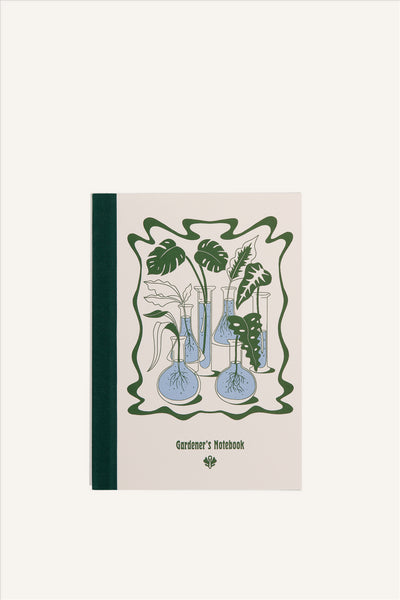 An A5 notebook with a beige cover and green cloth spine. The cover shows a green and blue illustration of a collection of glass flasks, all with different propagations and plant cuttings in them. The background of the image is beige.