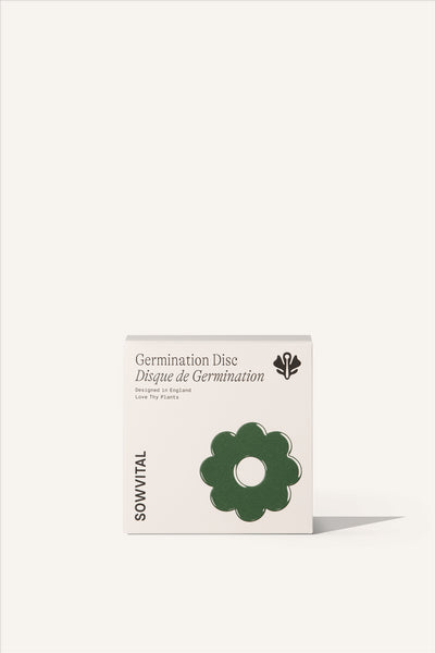 The Germination Disc box, a square beige fedrigoni paper box with a green embossed illustration of the flower shaped germination disc within. The background of the image is beige.