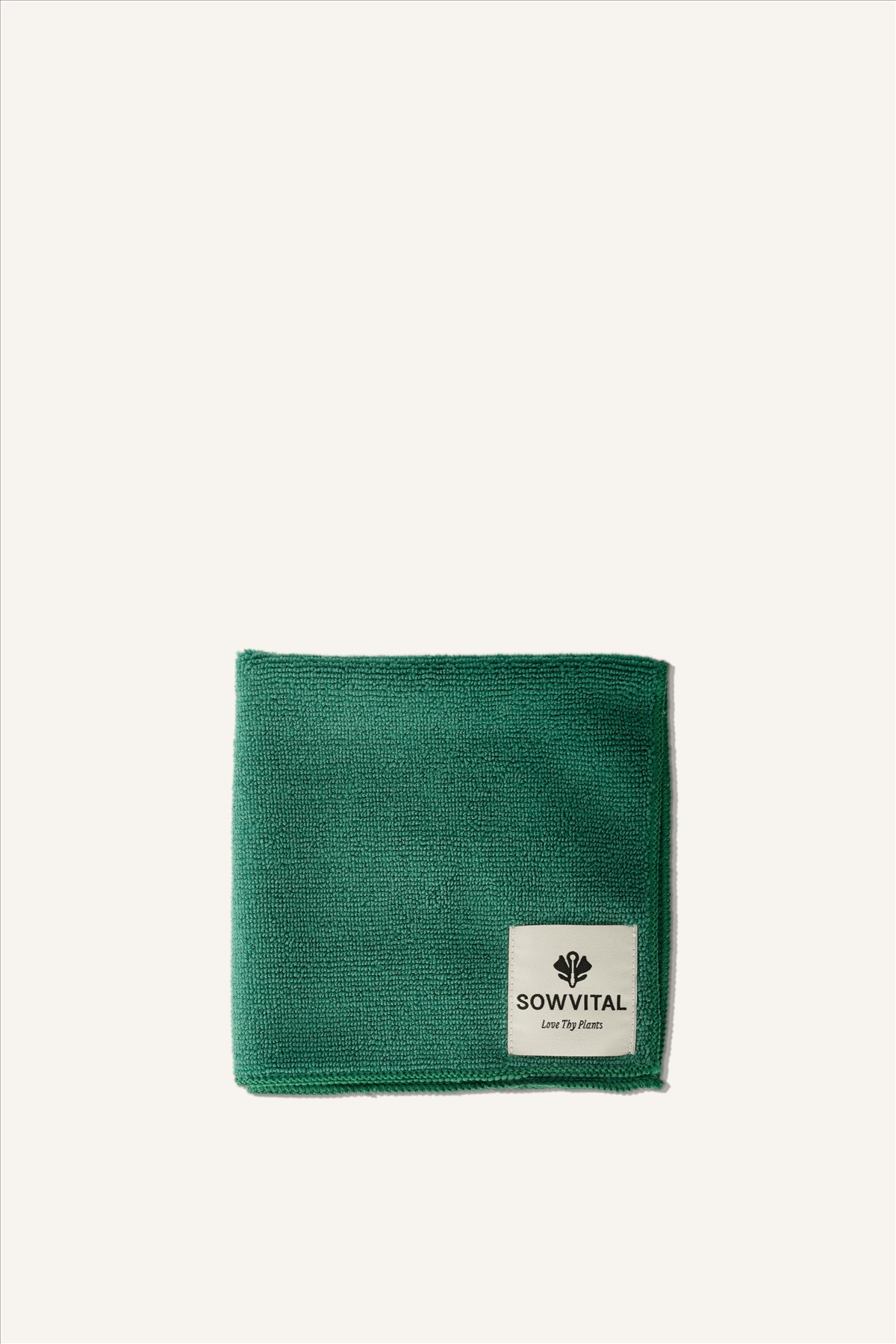 A soft looking green microfibre cloth, folded into a square. It has a beige label in the bottom right-hand corner, with the Sowvital logo in black and the phrase "Love Thy Plants". The background of the image is beige.