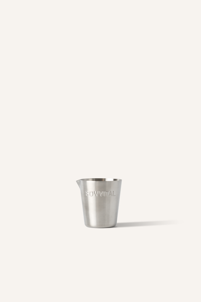 A stainless steel measuring cup with "SOWVITAL" stamped into the side, sat in front of a beige background.