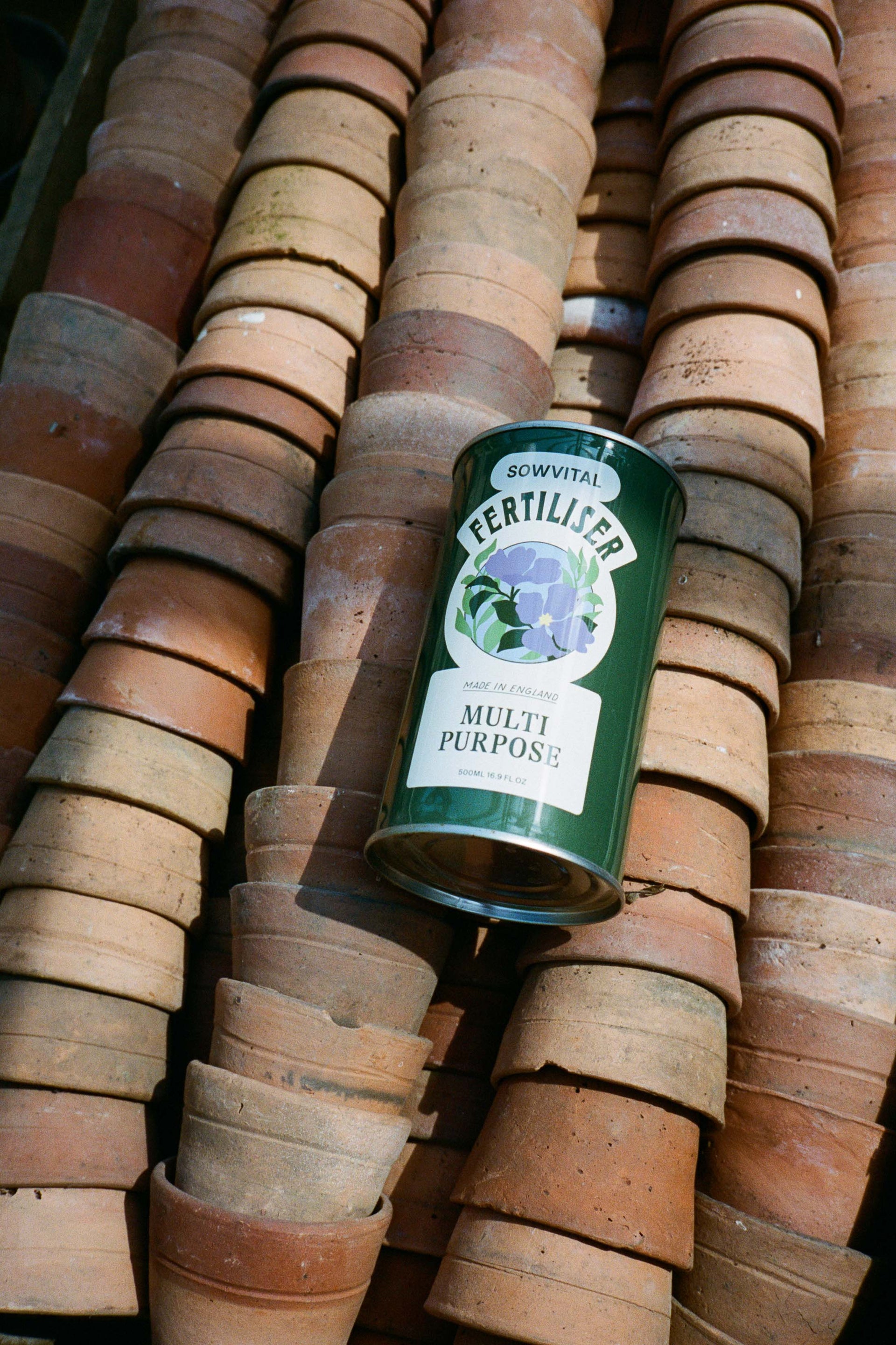 A green metal tin of Sowvital Multi Purpose fertiliser lays on top of rows of small stacked terracotta pots.