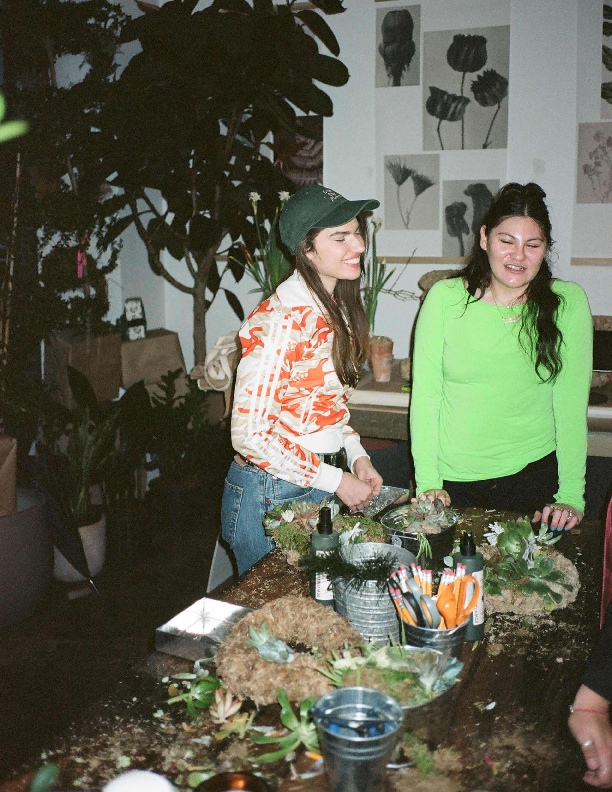 A photograph of people making themselves succulent wreaths while the table was covered with loads of materials and there were potted plants behind.