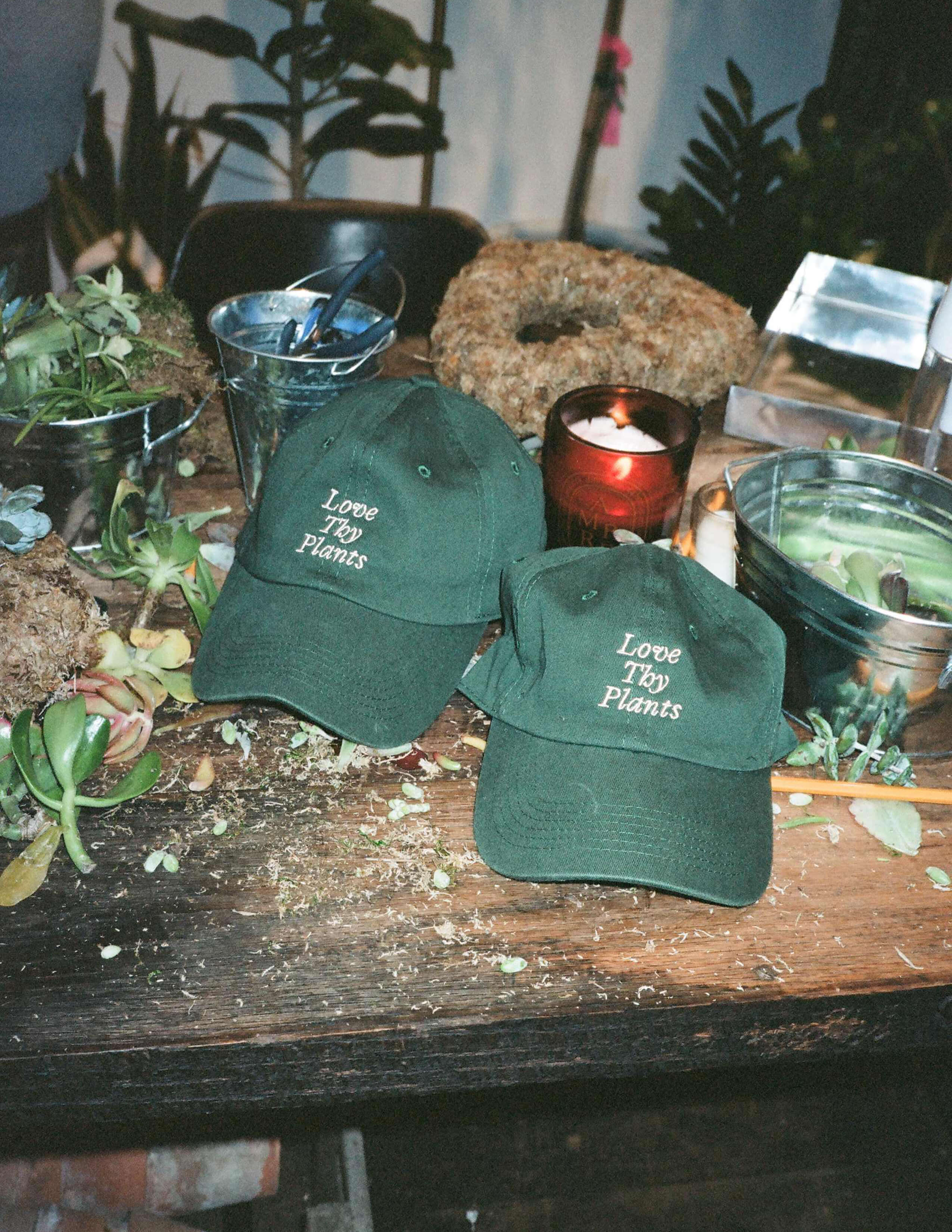 Two ‘Love Thy Plants’ caps with different kinds of materials for making wreaths on the table.