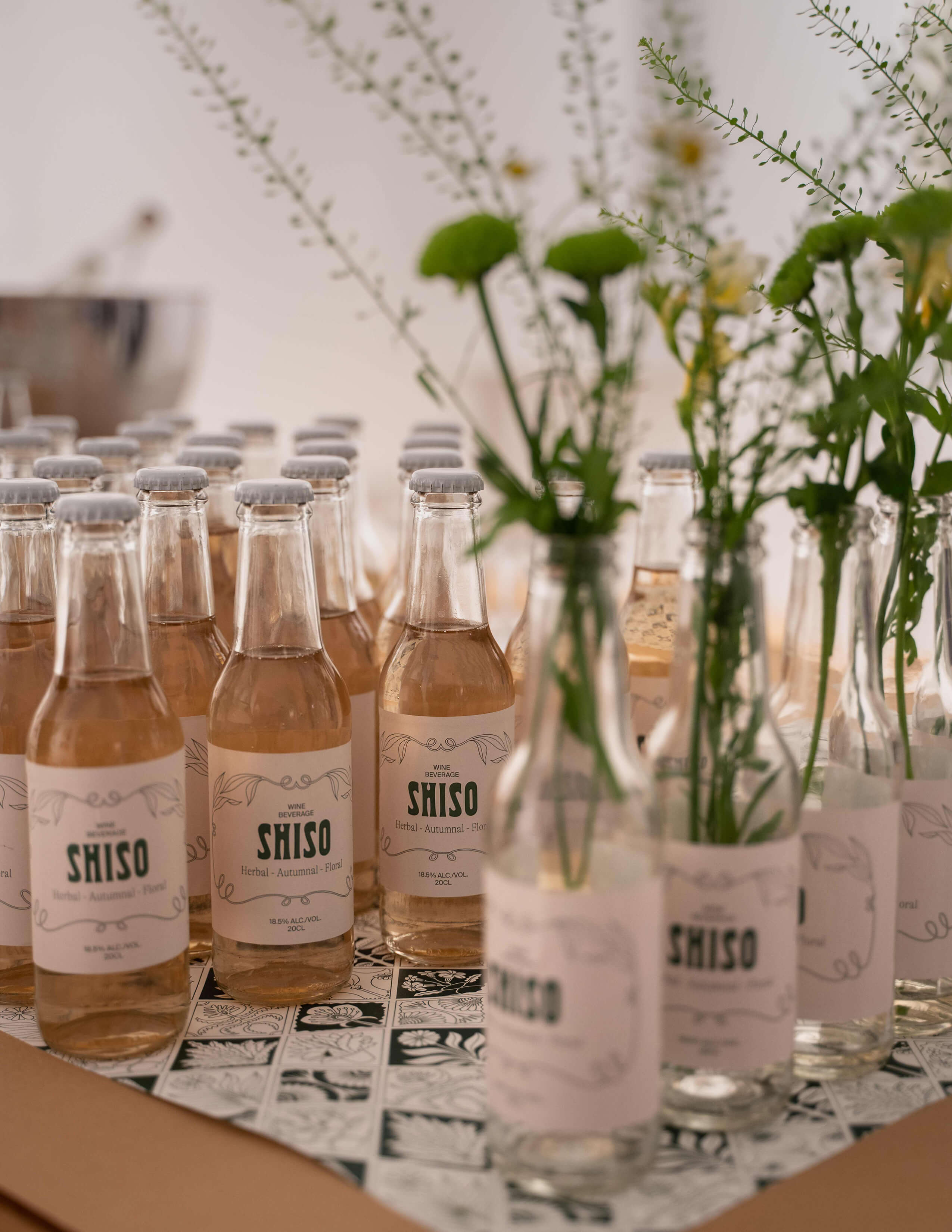 Plenty of bottles of Shiso, the alcoholic drink, are presented nicely on the table while there are some empty bottles filled with some plants and flowers.