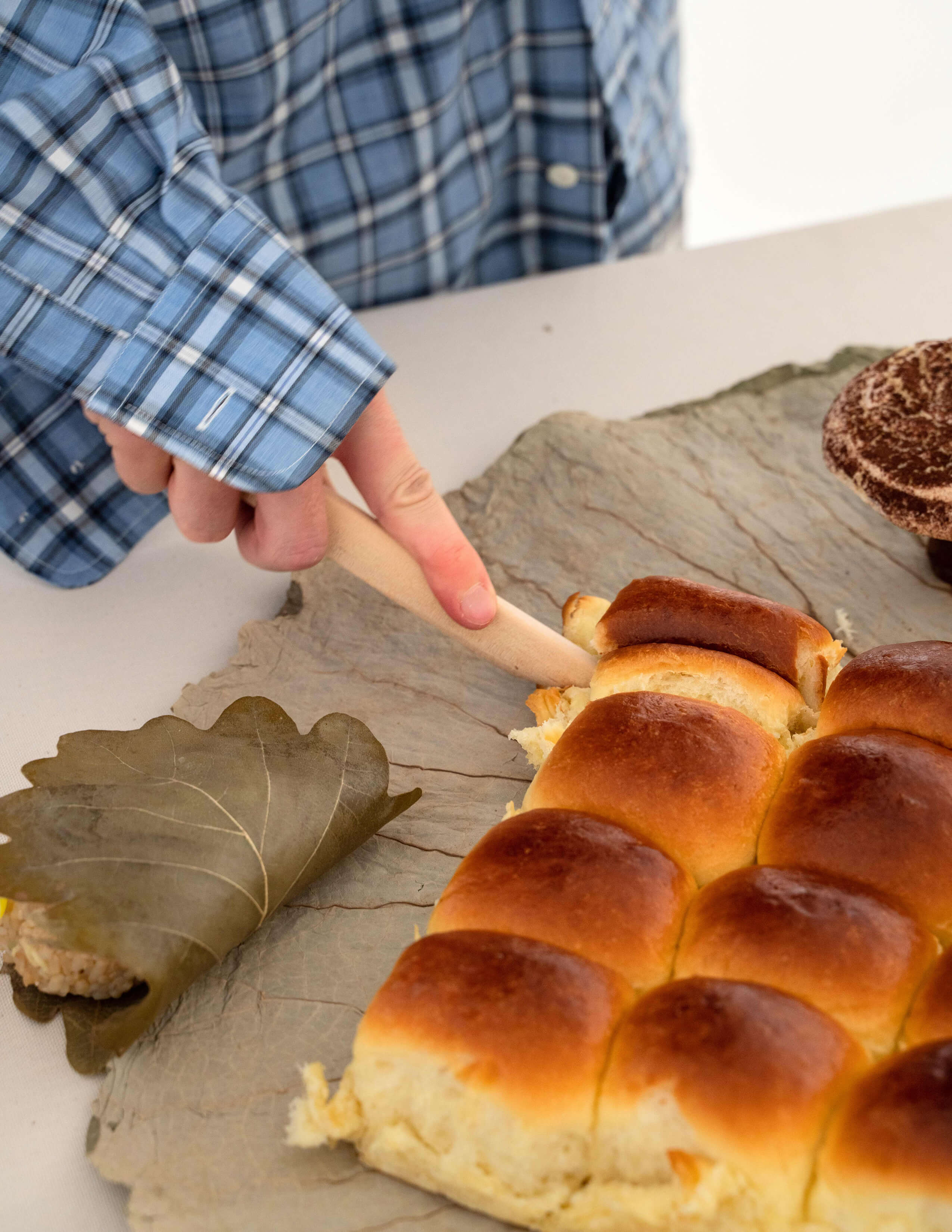 A person cuts the bread that is served on a big piece of leaf.