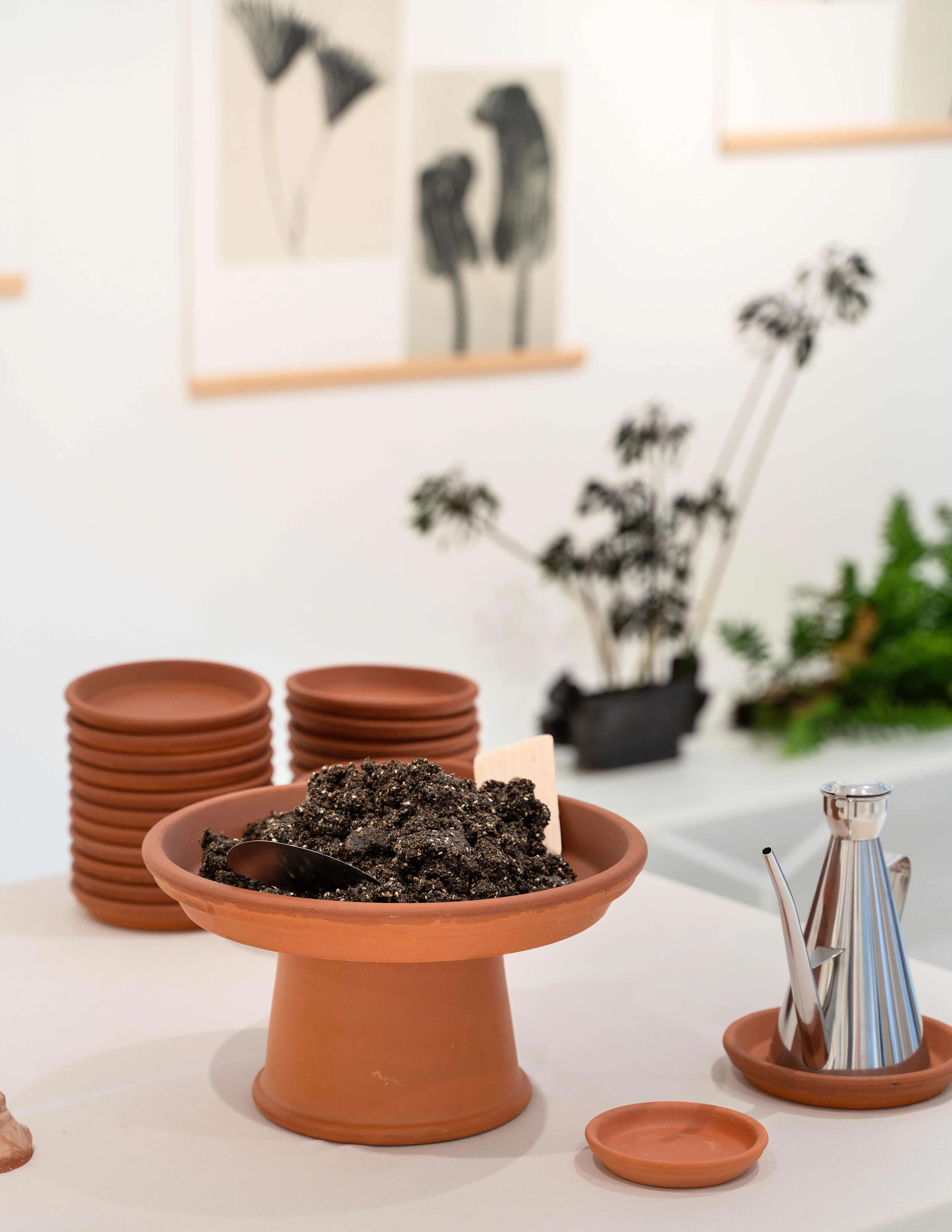 A plate of soil is presented next to a pile of small plates and a stainless steel oil pot.