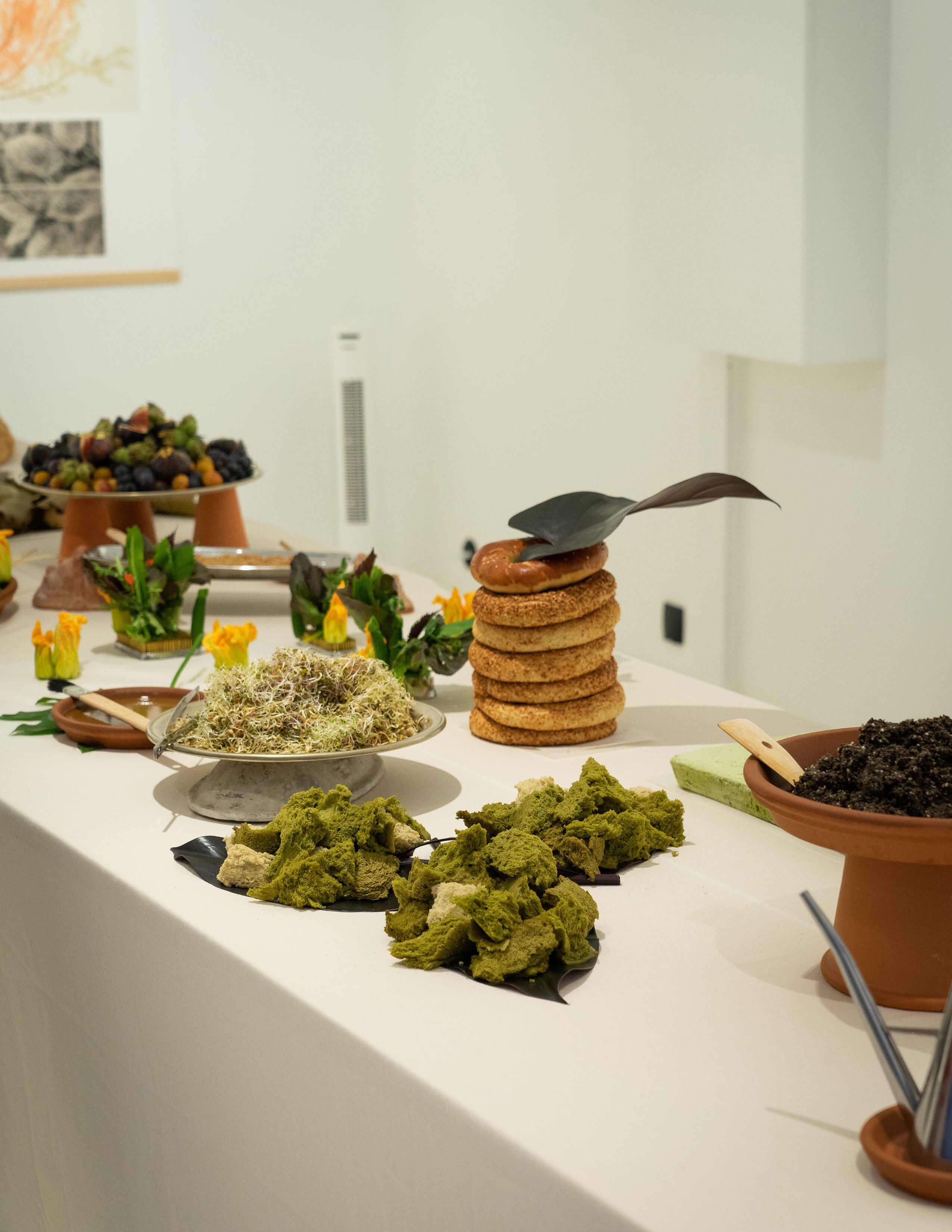 A collection of food is presented on the table.3 piles of ripped bread in green and cream, a plate of Alfalfa sprouts, a pile of bread covered with black and white sesame a piece of dark leaves on the top and many more.