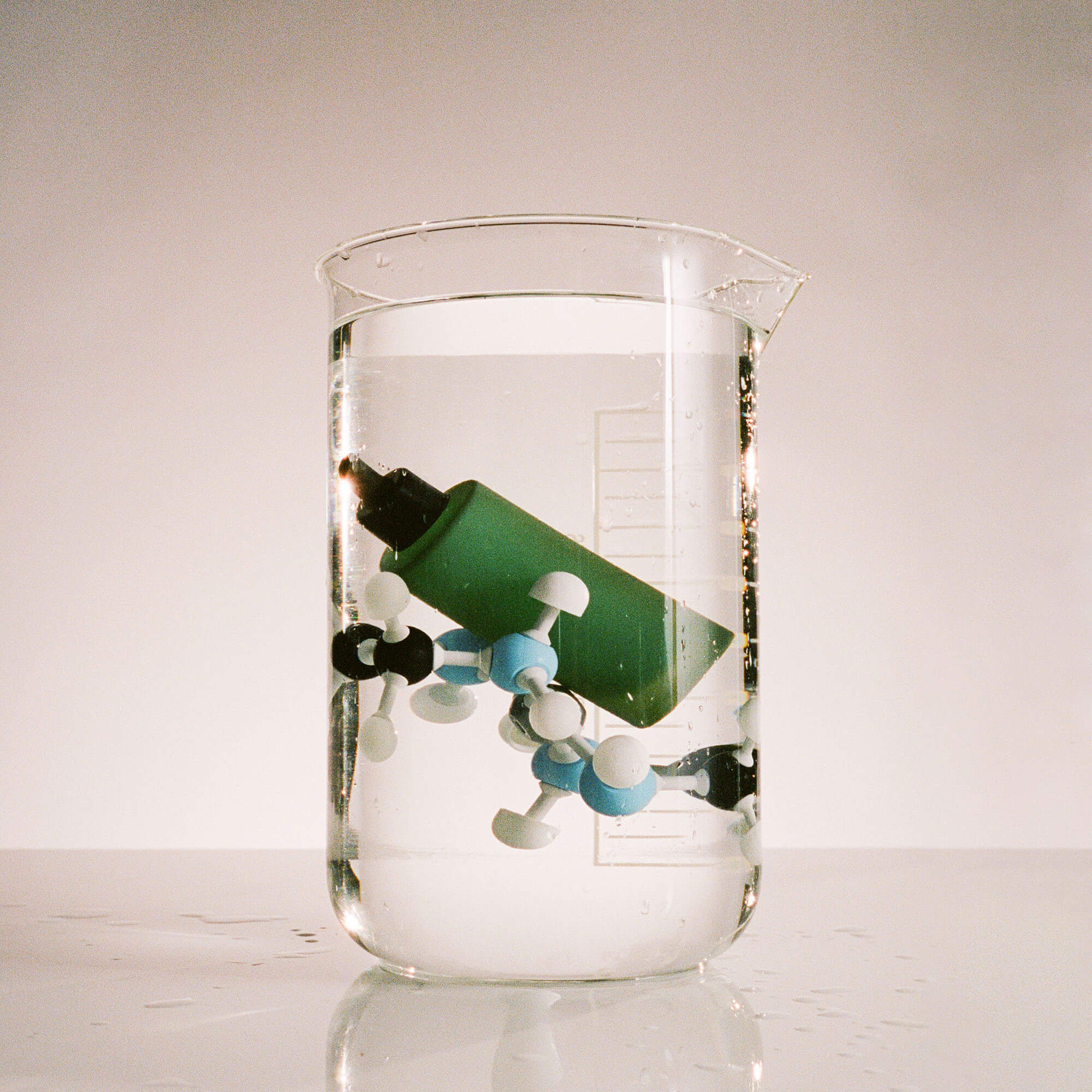 A glass flask filled with water, a House Plant Elixir bottle without its label, and a plastic representation of molecules.