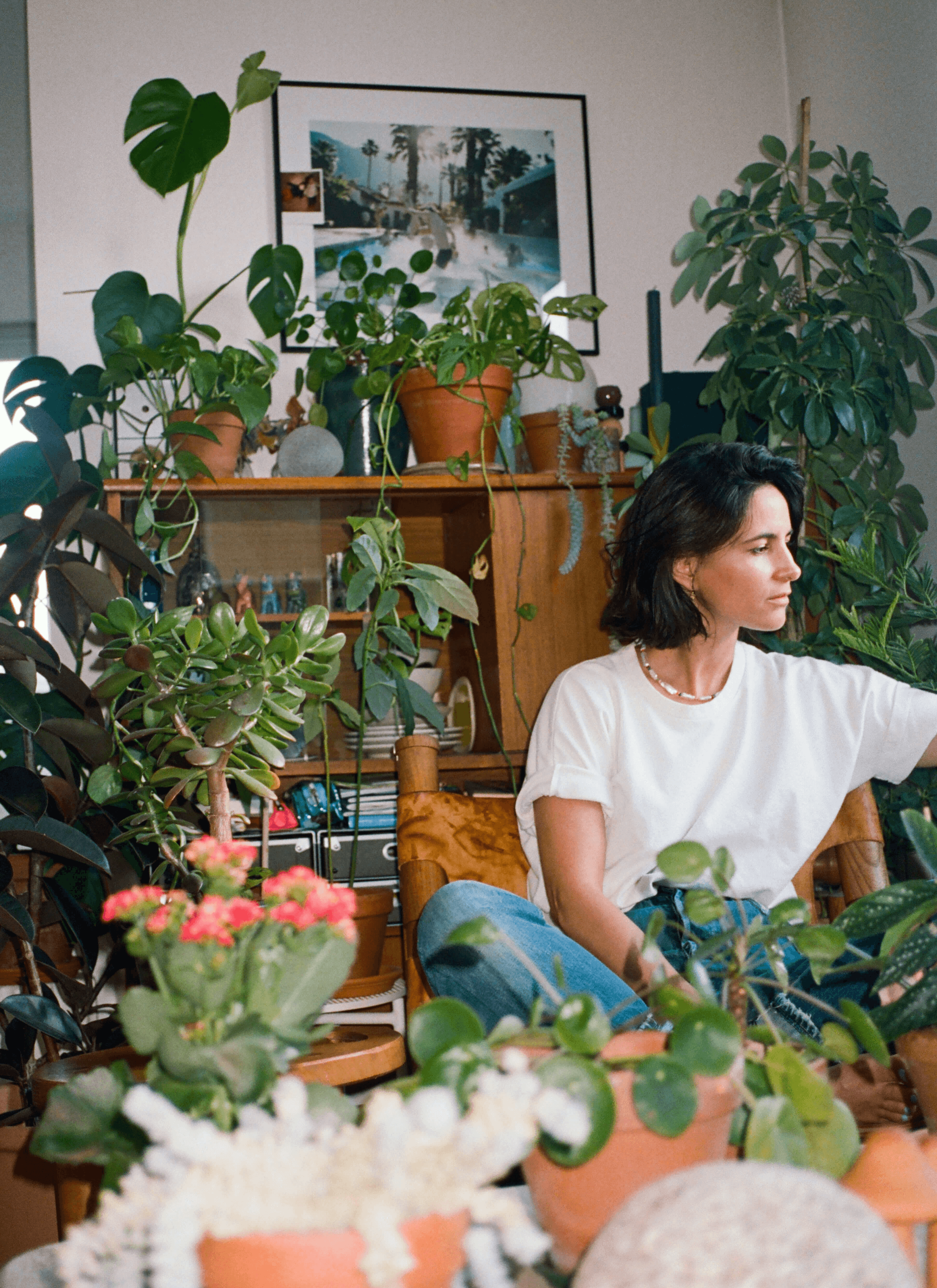 A photoshoot of Leslie David sitting in her studio surrounded by a collection of plants and flowers.