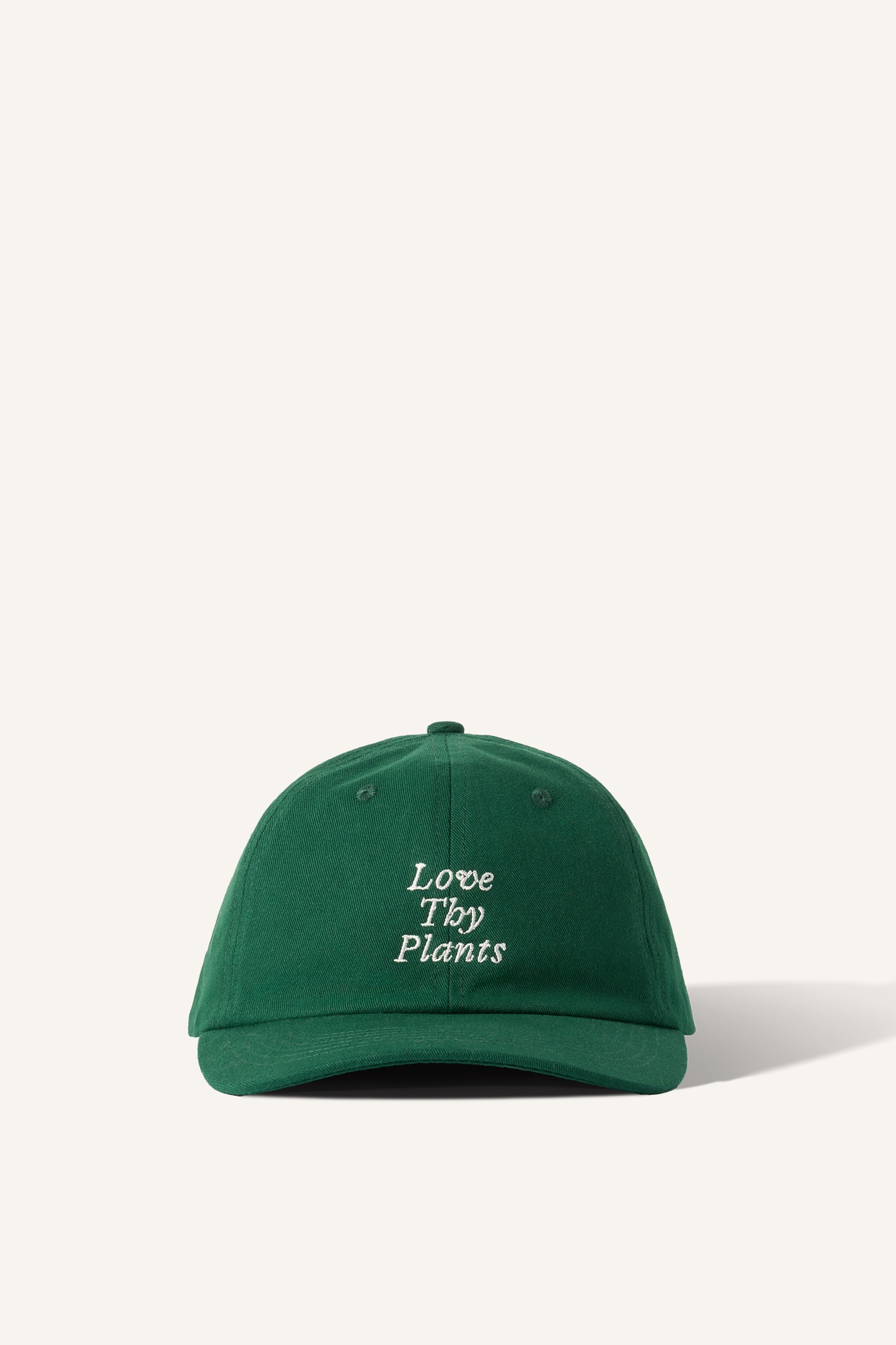 A green baseball cap, made of 100% cotton. Embroidered with the phrase "Love Thy Plants" on the front panel. The background is beige.